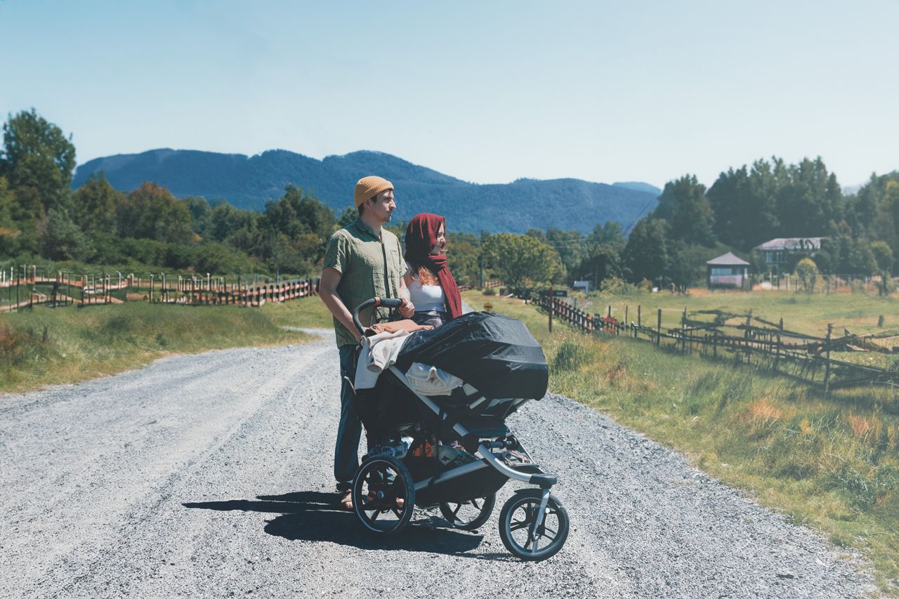 A couple enjoys a sunny day walk with their baby carriage on a rural path.